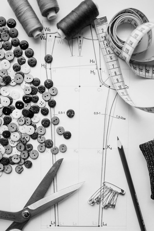 Photo noire et blanc d’une pièce de patron en papier, entourée d’accessoires de couture